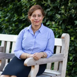 Kavita Kumari sitting on bench with leafy bush in background
