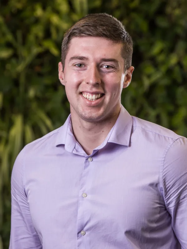 Niall Conyers head and shoulders image while wearing a lilac shirt in front of a greenery backdrop