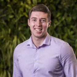Niall Conyers head and shoulders image while wearing a lilac shirt in front of a greenery backdrop