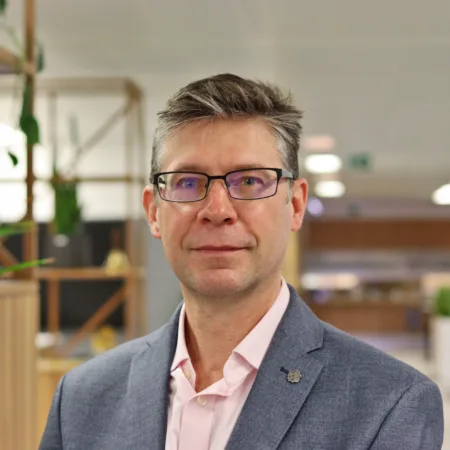 Paul in a grey blazer and ppink shirt with the office blurred in the background