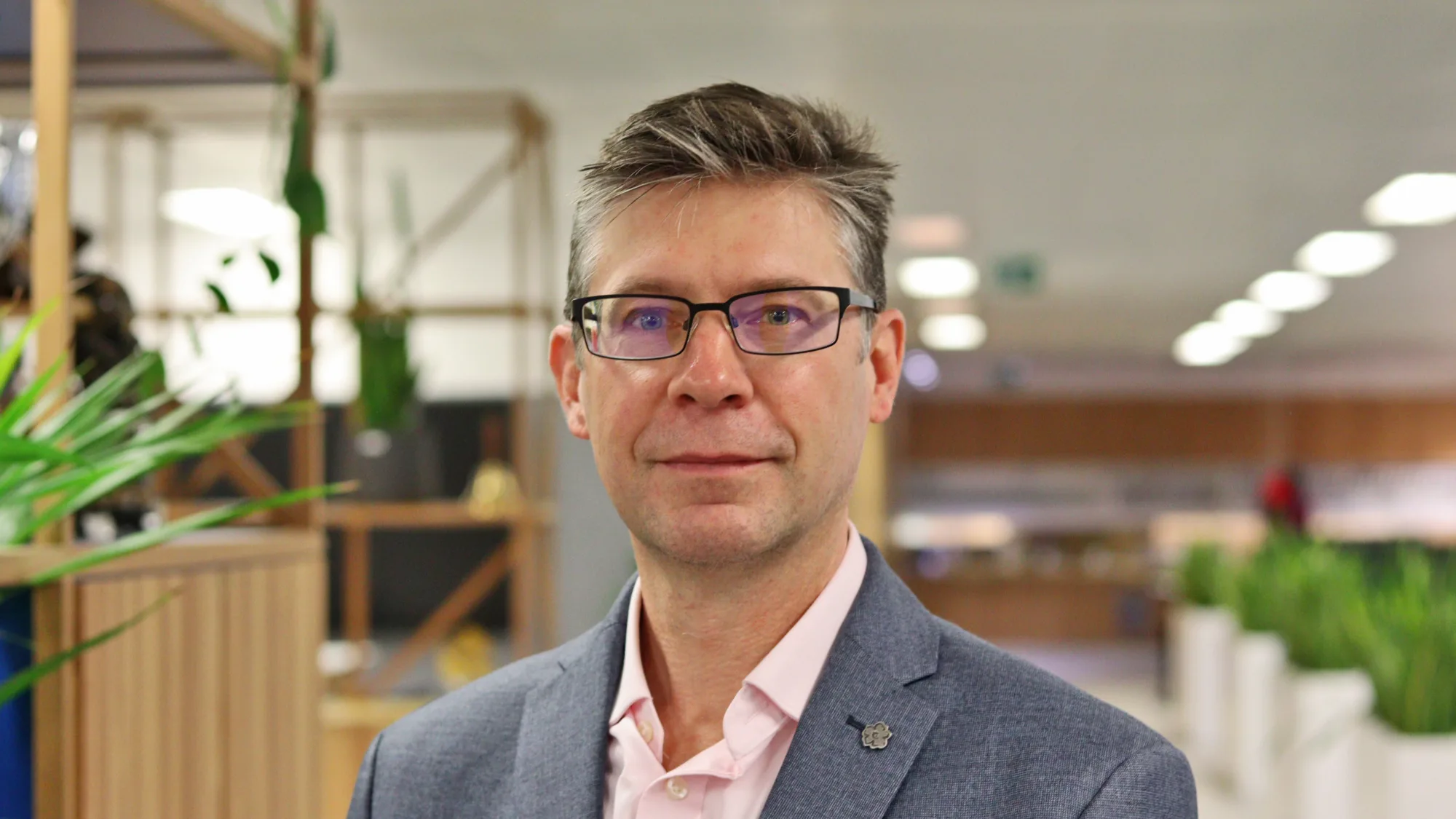Paul in a grey blazer and ppink shirt with the office blurred in the background