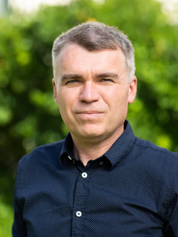 Head and sholders shot of Rasti wearing a dark blue shirt against green foliage