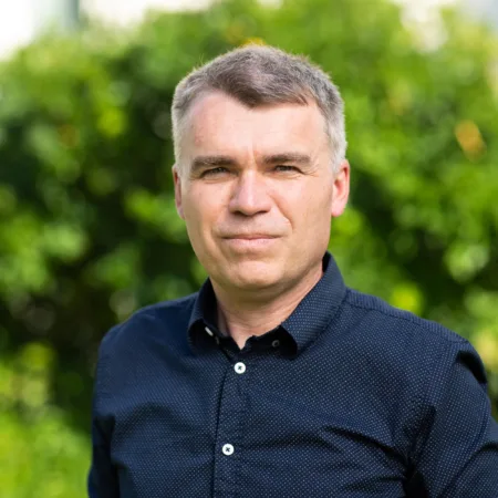 Head and sholders shot of Rasti wearing a dark blue shirt against green foliage