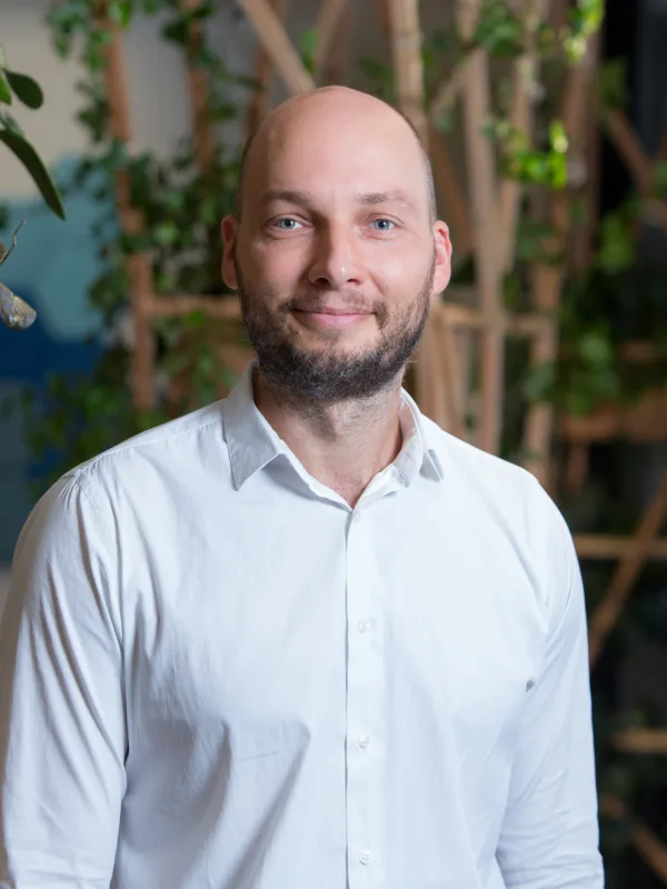 Rytis smiling to camera stood in front of a wooden trellis with plants