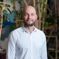 Rytis smiling to camera stood in front of a wooden trellis with plants