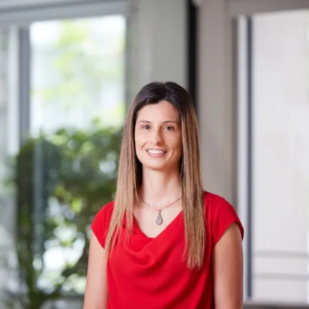 Valeria Riso smiling towards the camera in a red top against a blurred background of the London office