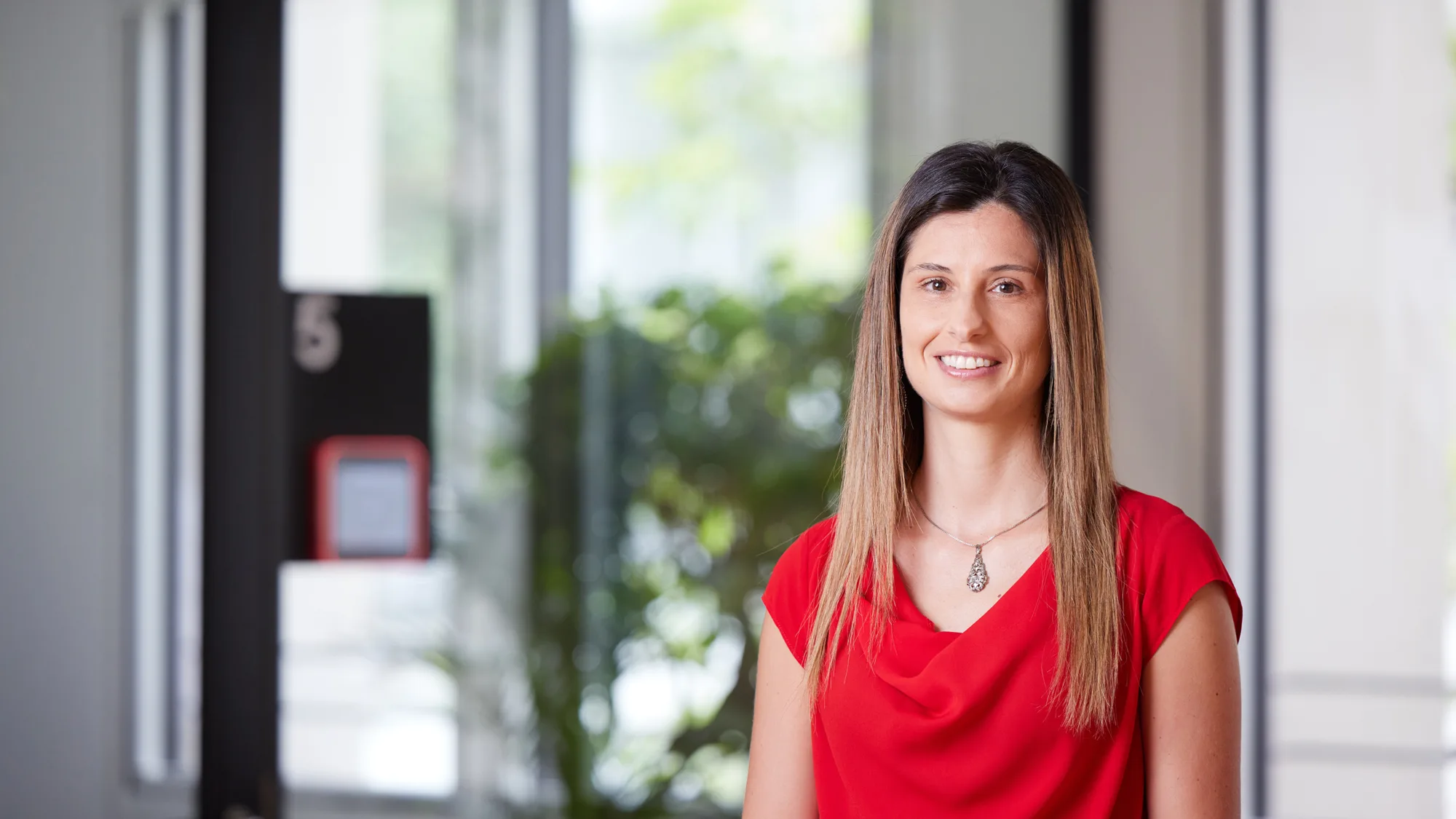 Valeria Riso smiling towards the camera in a red top against a blurred background of the London office