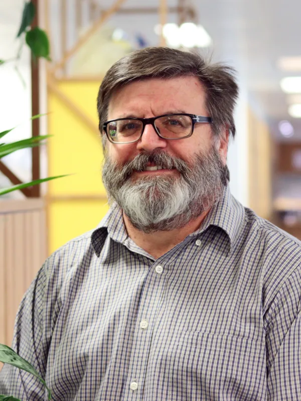 Wayne in an open collar shirt stood in an open plan office