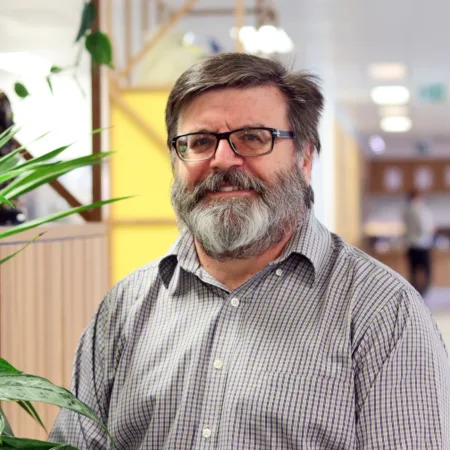 Wayne in an open collar shirt stood in an open plan office