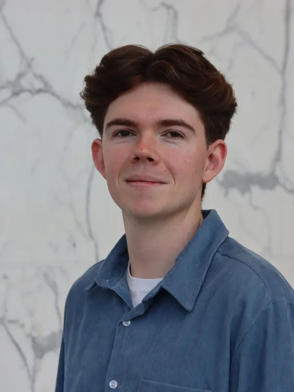Zac in a blue open collar shirt with a white t-shirt underneath in front of a marbled wall.