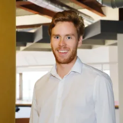 Jamie in a white open collar shirt smiling to camera in the Cundall Birmingham office