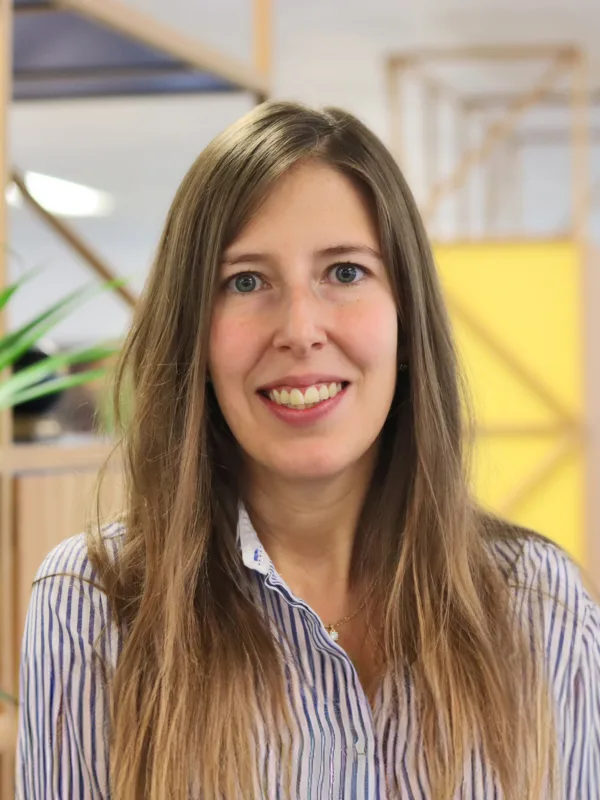 Head and shoulders portrait of Marta Hergueta Ortega wearing a stripy buttoned shirt with an office setting behind.