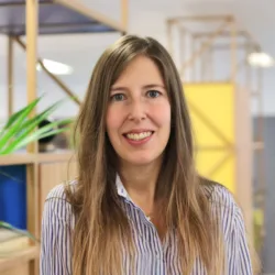 Head and shoulders portrait of Marta Hergueta Ortega wearing a stripy buttoned shirt with an office setting behind.