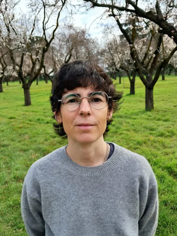 Head and sholders shot of Lucia wearing a grey jumper agaist a back drop of trees