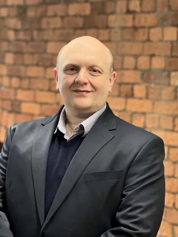 Andy in a dark suit in front of a brick wall