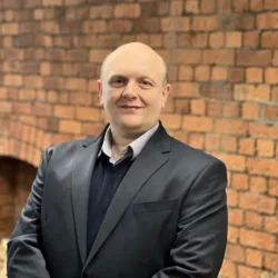 Andy in a dark suit in front of a brick wall
