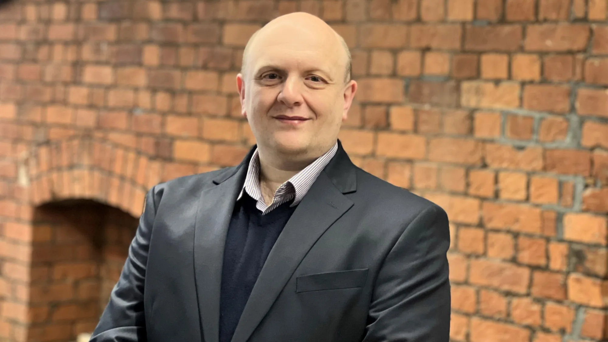 Andy in a dark suit in front of a brick wall