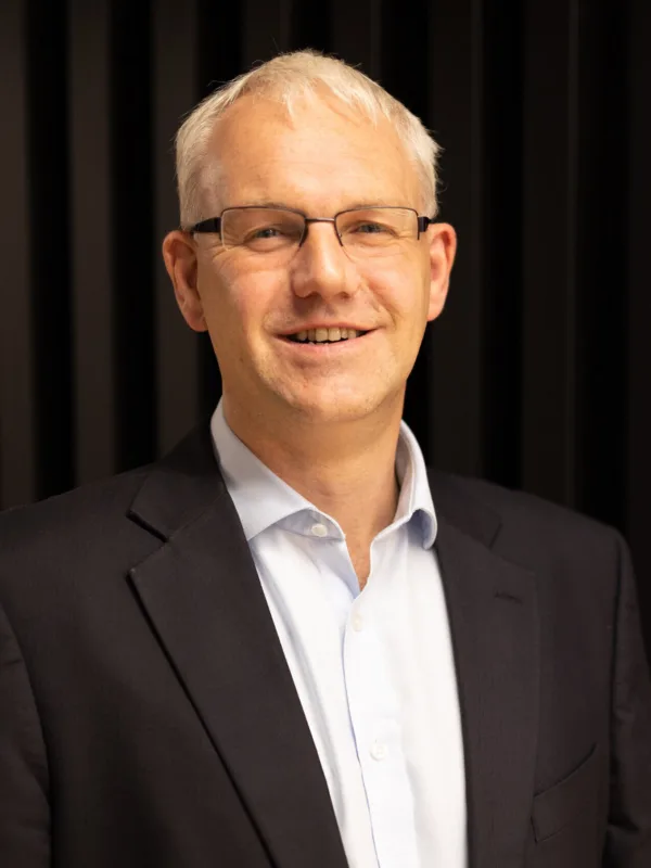Graham in an open collar shirt and suit jacket against a dark wall