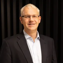Graham in an open collar shirt and suit jacket against a dark wall