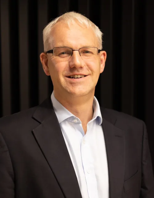 Graham in an open collar shirt and suit jacket against a dark wall