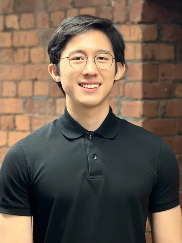 Jerryl in a black polo t-shirt in front of an internal brick wall