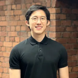 Jerryl in a black polo t-shirt in front of an internal brick wall