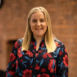 Liz Skelton wearing a floral shirt and standing in front of bricked wall interior
