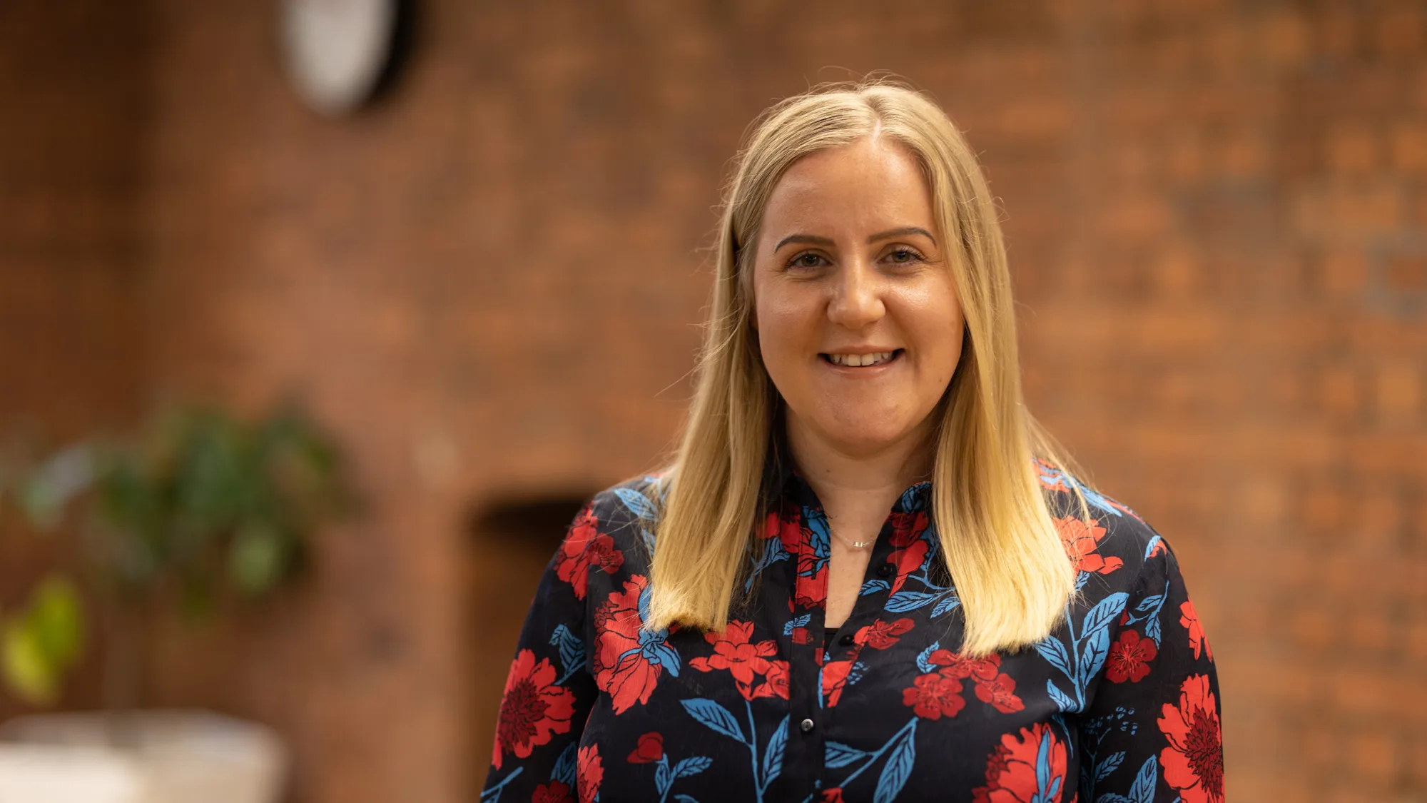 Liz Skelton wearing a floral shirt and standing in front of bricked wall interior