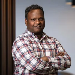 Headshot of Priyatharsan taken inside office with blurred background showing office interior and lighting.