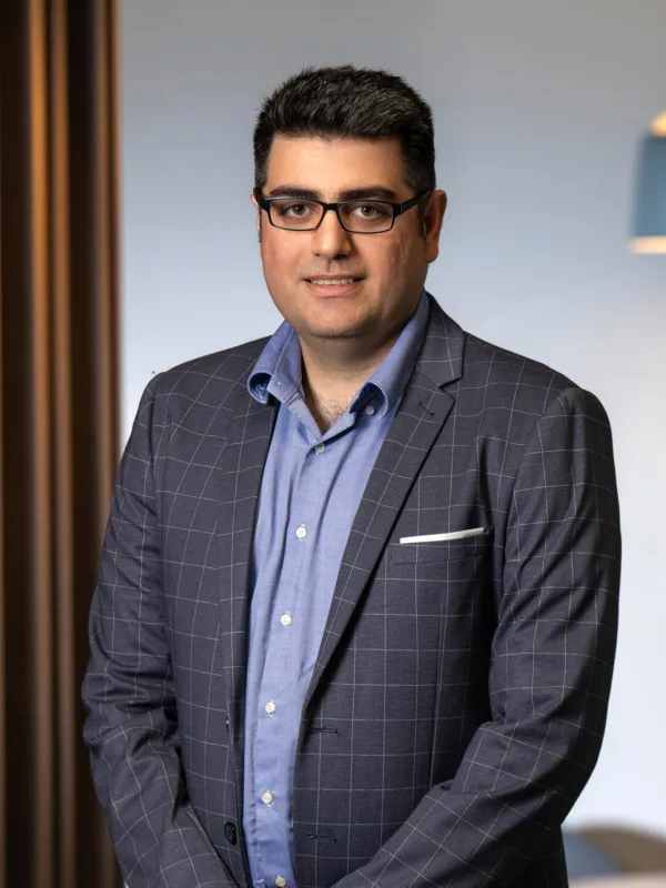 Vahid smiling at camera standing in front of wooden panelling in office