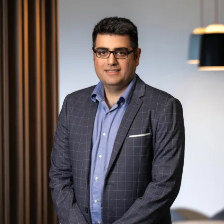 Vahid smiling at camera standing in front of wooden panelling in office