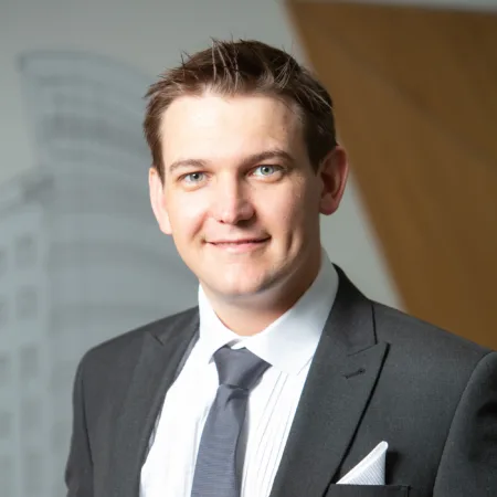 Barrie in a shirt tie and jacket smiling to camera in front of a vinyled office wall