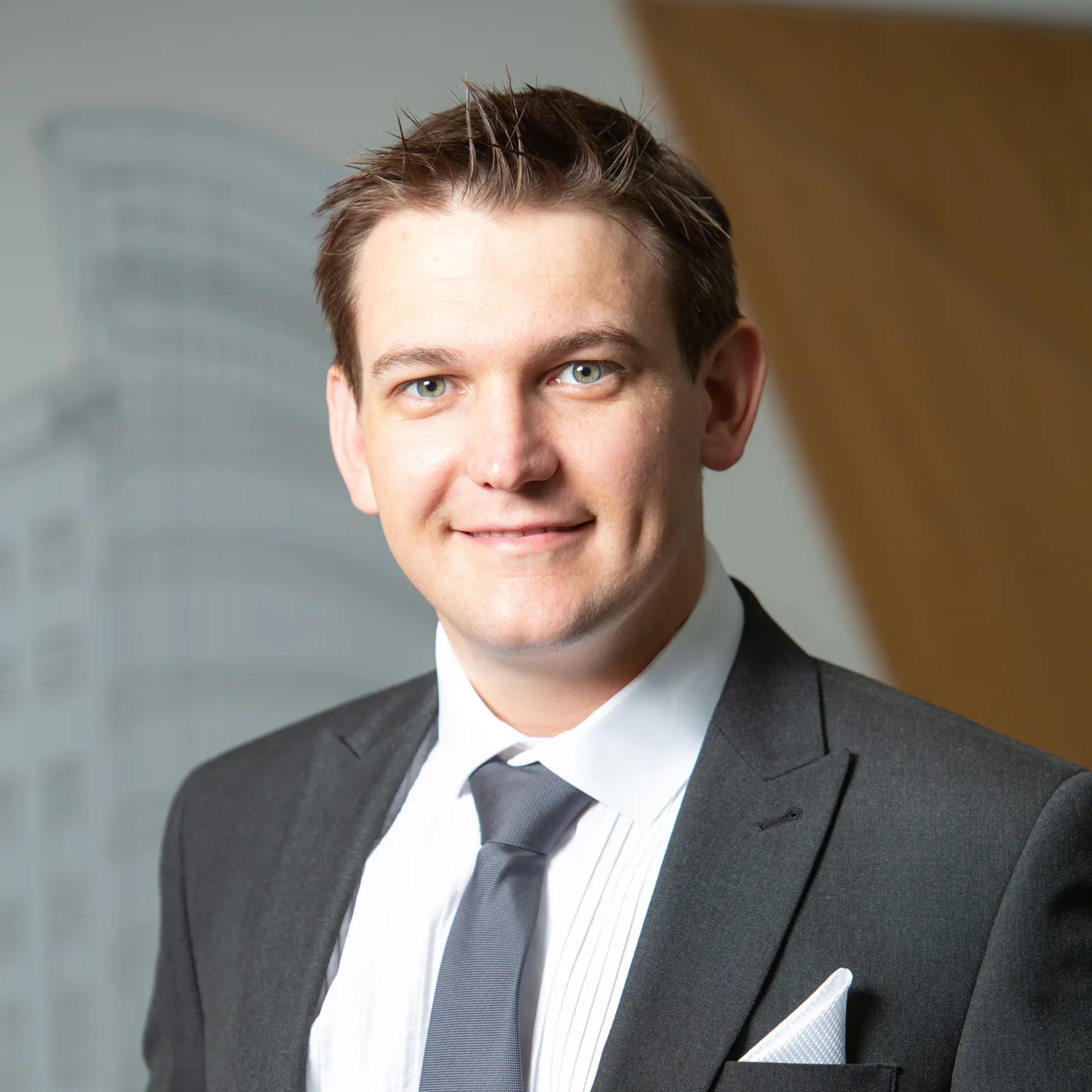 Barrie in a shirt tie and jacket smiling to camera in front of a vinyled office wall
