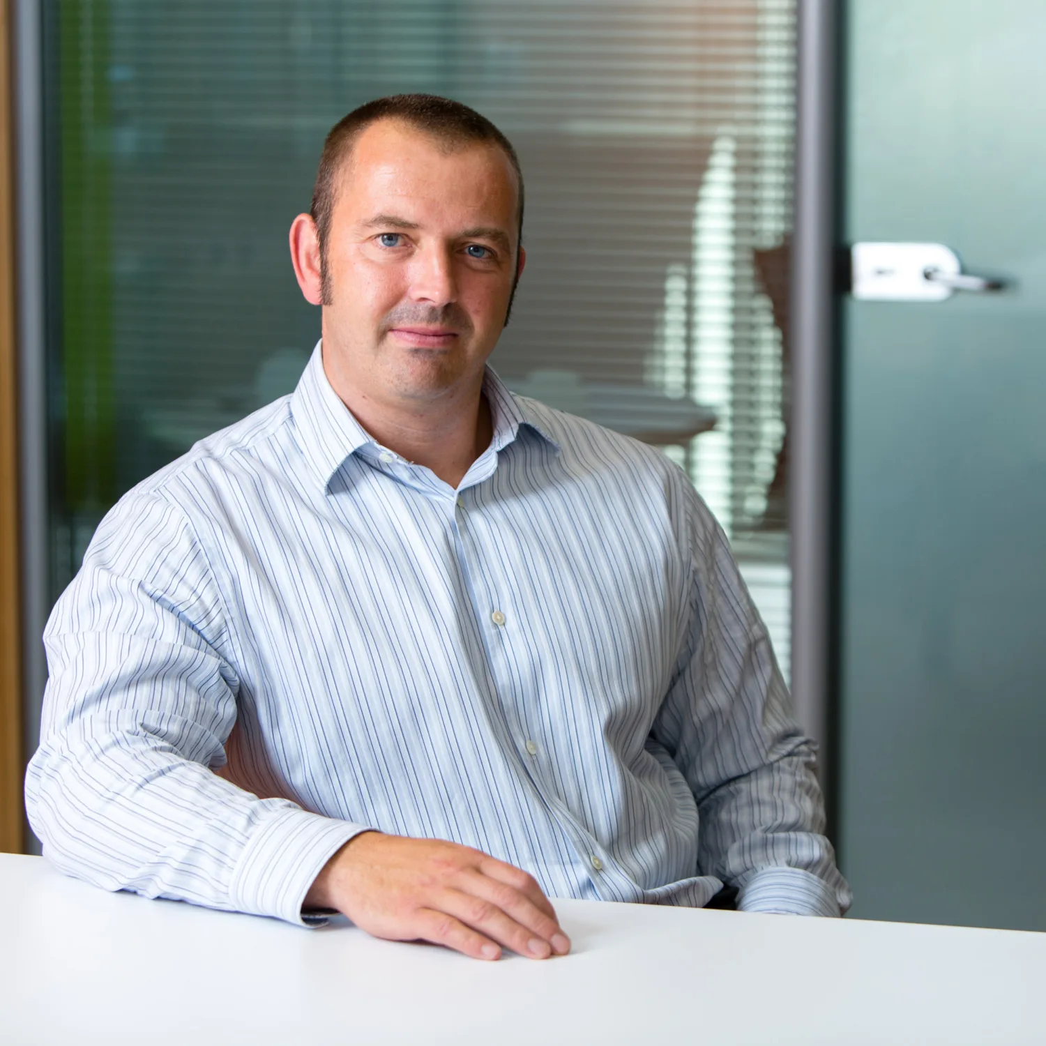 Gary Marshall in a chair at a desk in a white shirt, with glass meeting room frontage behind him