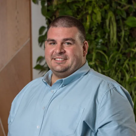 Michael in a light green open collar shirt smiling in front of a living wall