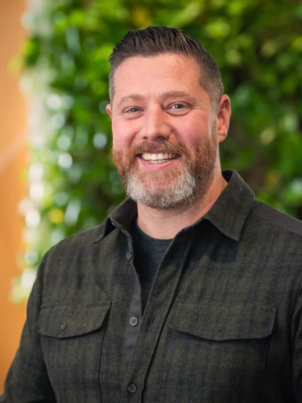 Head and shoulders shot of Oliver wearing a dark shirt against a green and brown background