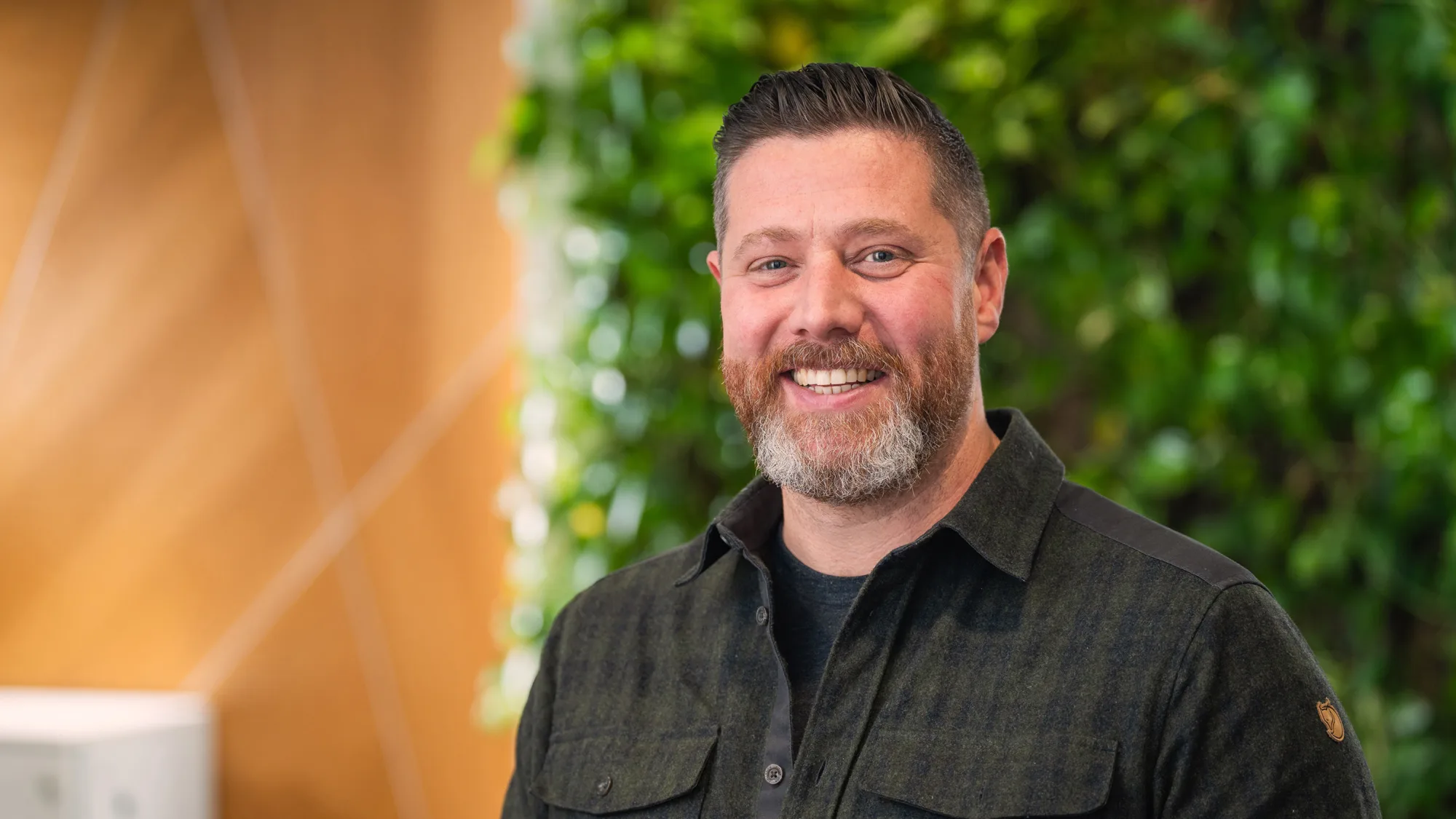 Head and shoulders shot of Oliver wearing a dark shirt against a green and brown background