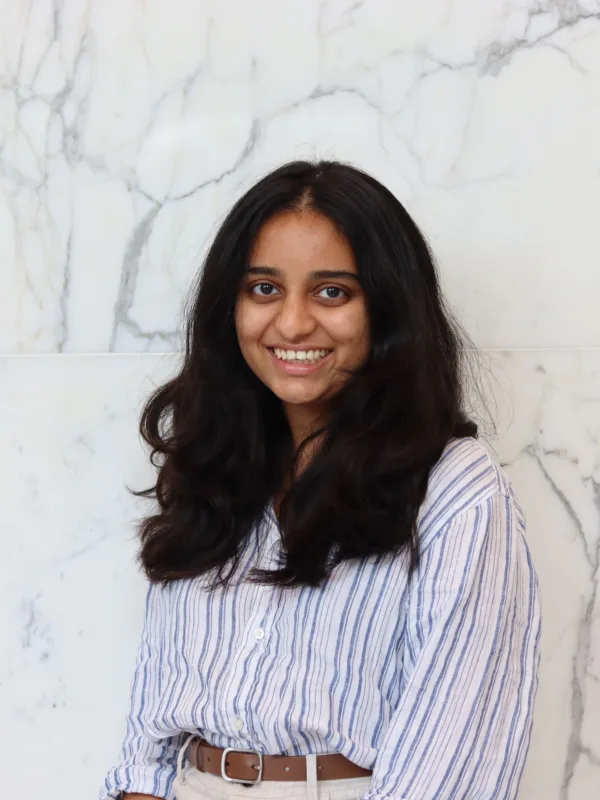 Portrait of a person with long dark hair wearing a blue and white striped shirt against a white marble wall.