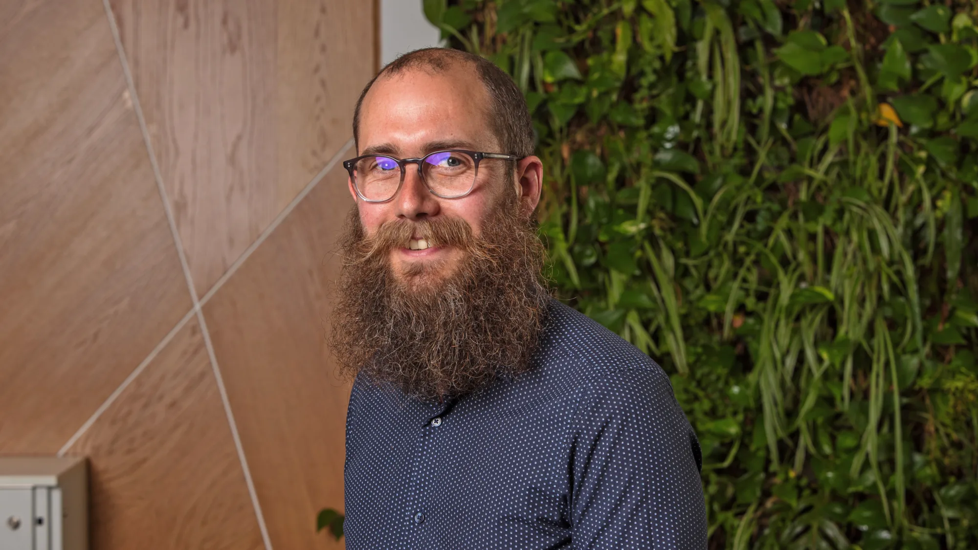 Steven in a dark blue shirt in front of a wooden panel and green living wall