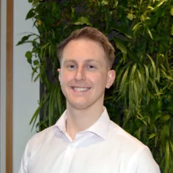 Tom in a white open collared shirt in front of a living wall