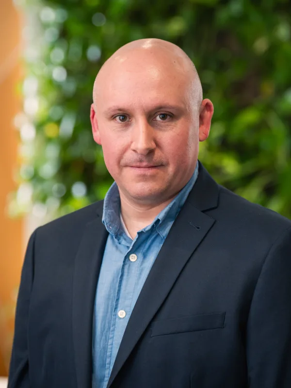 Tony looking to camera in an open collar shirt and suit jacket in front of a living wall