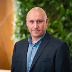 Tony looking to camera in an open collar shirt and suit jacket in front of a living wall