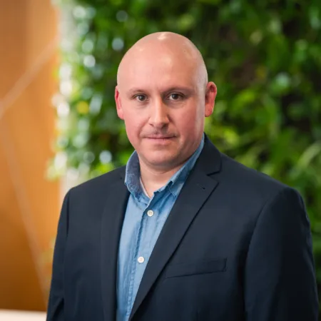 Tony looking to camera in an open collar shirt and suit jacket in front of a living wall