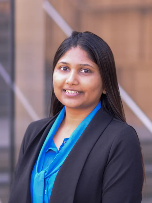 Head and sholders shot of Ankita wearing a bright blue shirt and dark blue blazer standing against a brown background