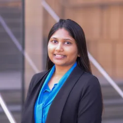 Head and sholders shot of Ankita wearing a bright blue shirt and dark blue blazer standing against a brown background