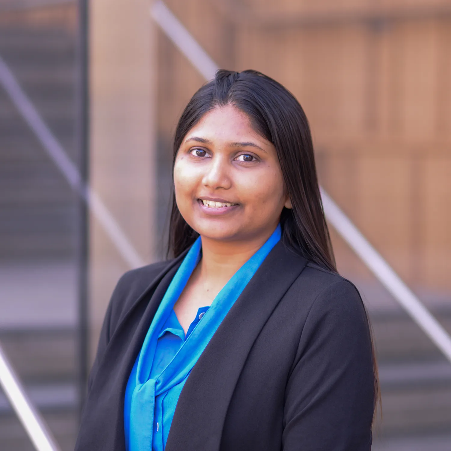 Head and sholders shot of Ankita wearing a bright blue shirt and dark blue blazer standing against a brown background