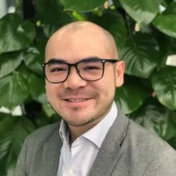 Head and Shoulders shot of Marcus wearing glasses sitting in front of plants