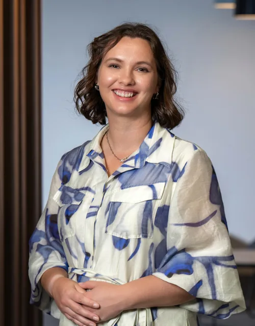 Joanne Sim in a white and blue dress with the office reception area and chair in the background