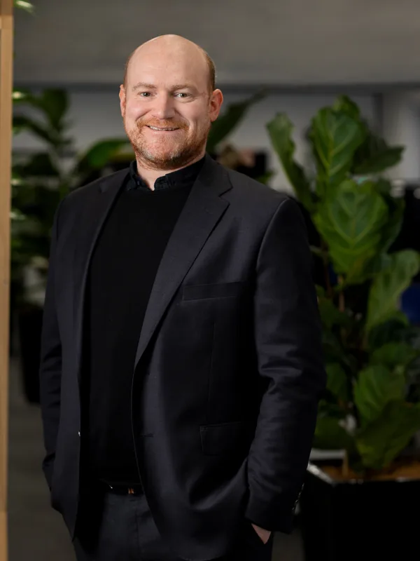 Jordan wearing a black suit standing in front of a plant