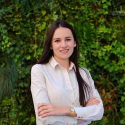 Person in a light shirt standing with arms crossed in front of a green living wall.